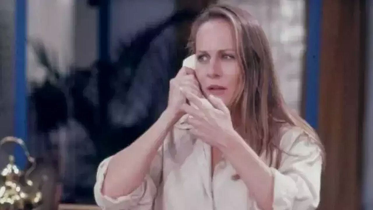 Mulher de cabelo longo segura telefone com expressão preocupada dentro de casa
