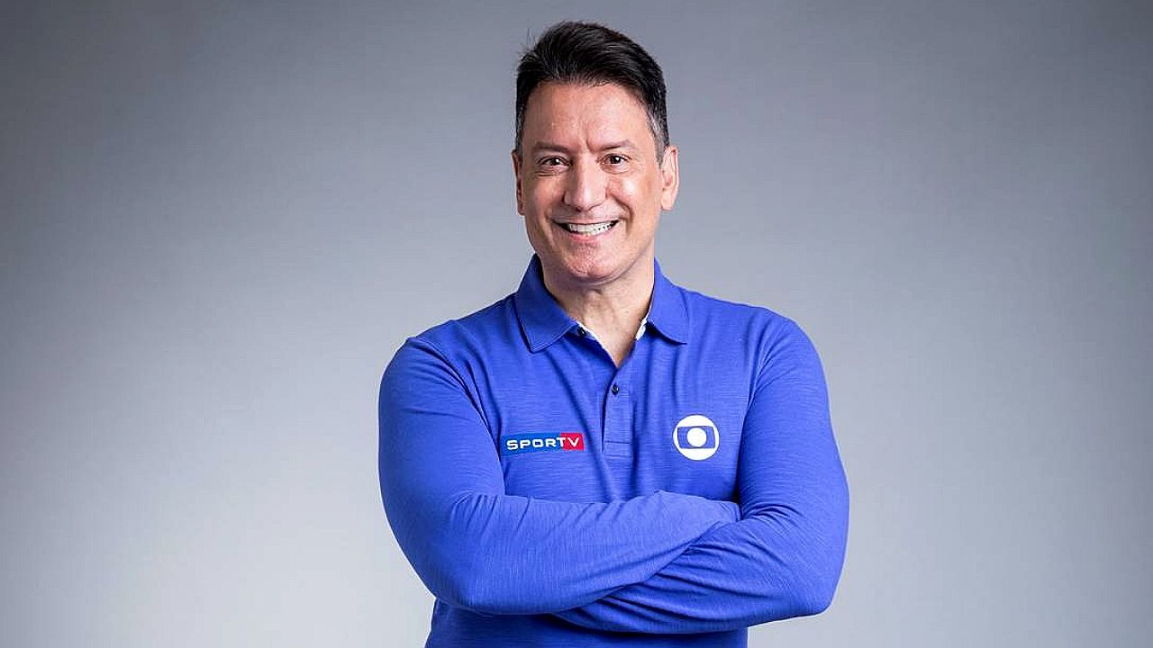 Luiz Carlos Jr. sorri com braços cruzados usando camisa da Globo e do sportv em foto promocional da emissora