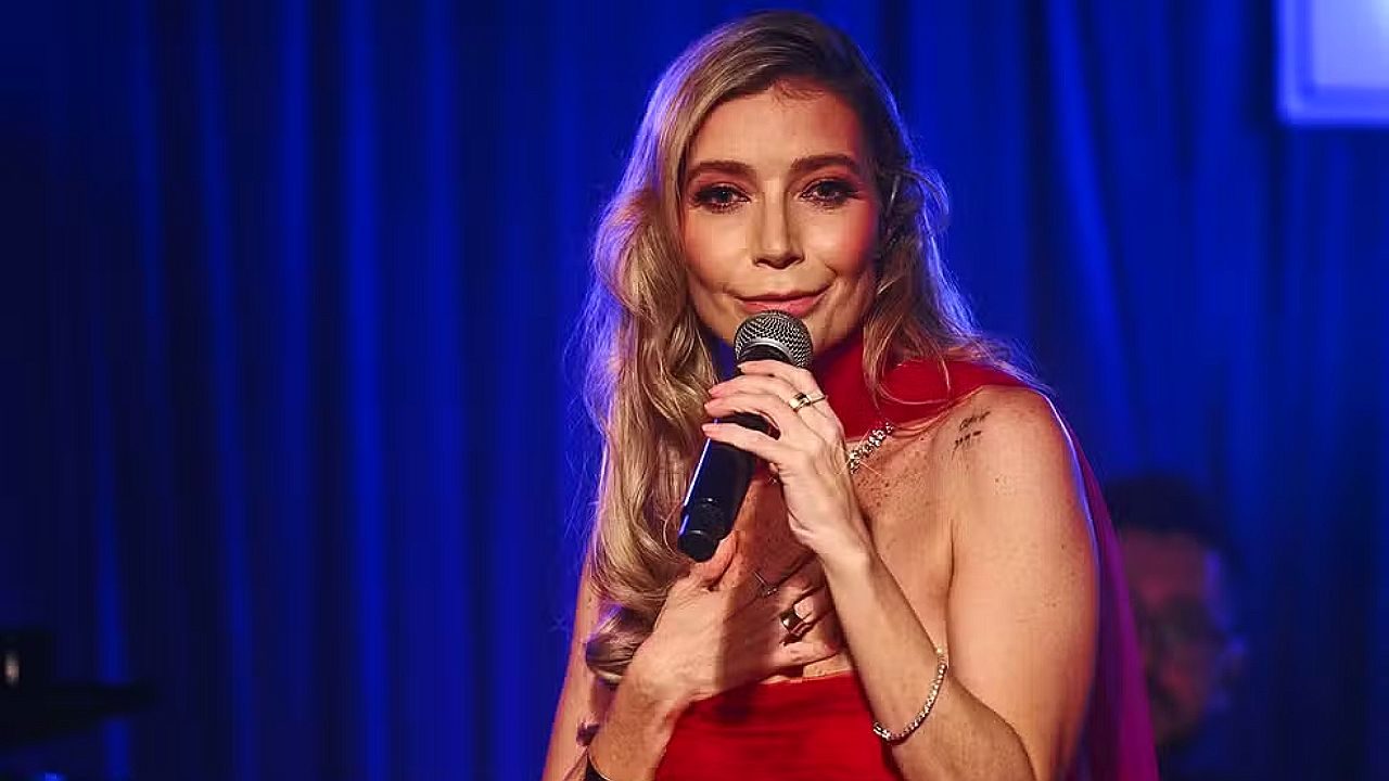 Luiza Possi canta ao microfone com vestido vermelho durante apresentação em palco iluminado