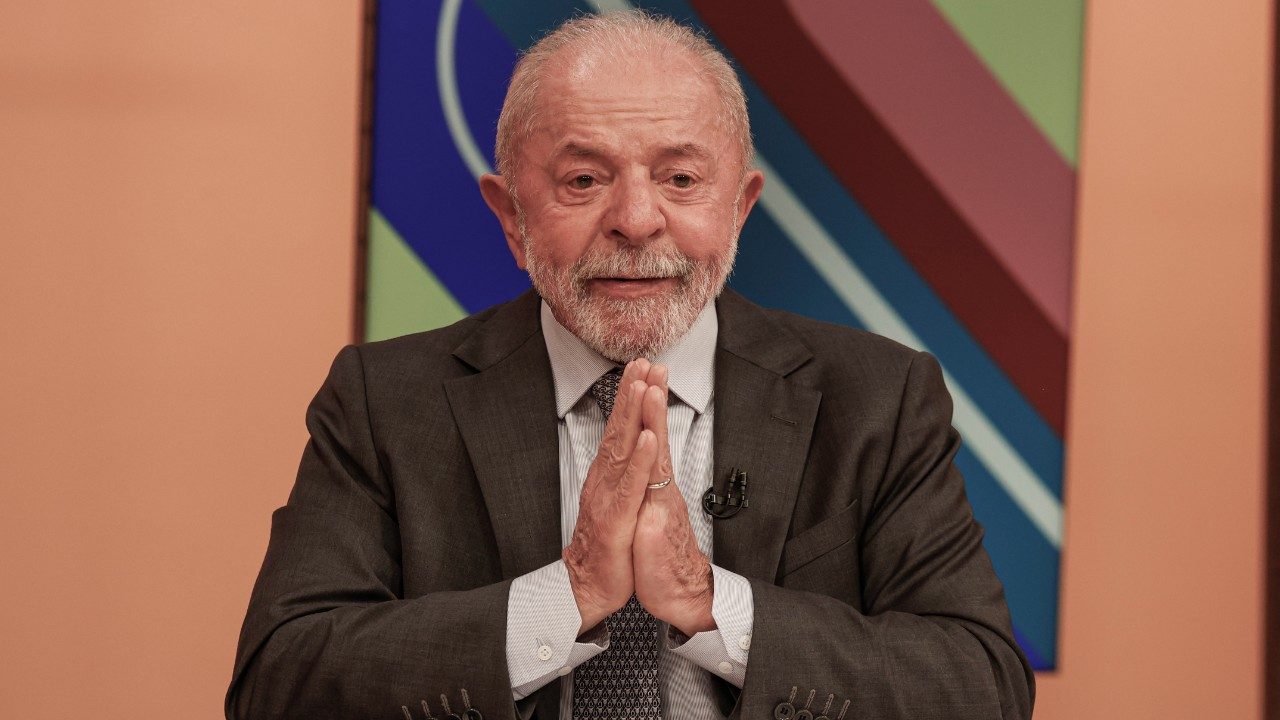 Luiz Inácio Lula da Silva com mãos unidas durante participação no programa Sem Censura em cenário colorido da TV Brasil