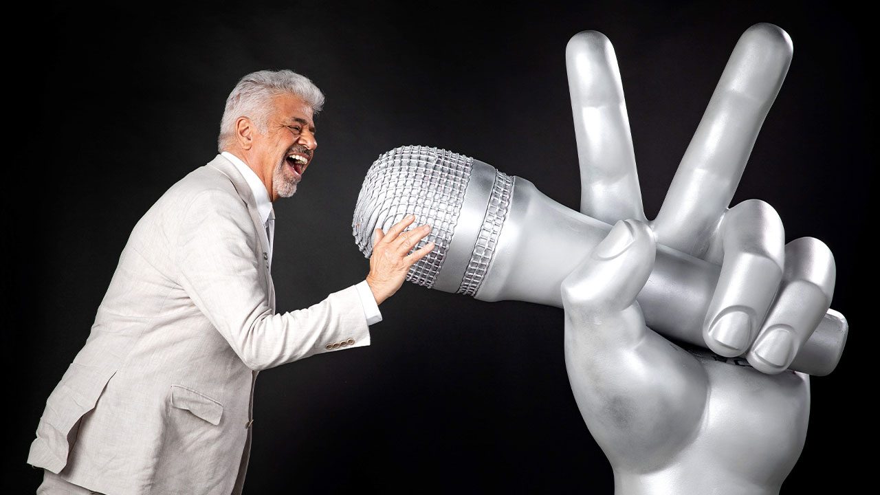 Lulu Santos sorrindo ao lado do microfone gigante em formato de mão do The Voice Brasil na Globo