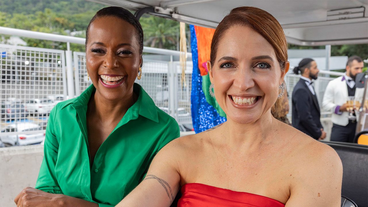 Maju Coutinho de camisa verde e Poliana Abritta de vestido vermelho sorrindo juntas nos bastidores dos Estúdios Globo