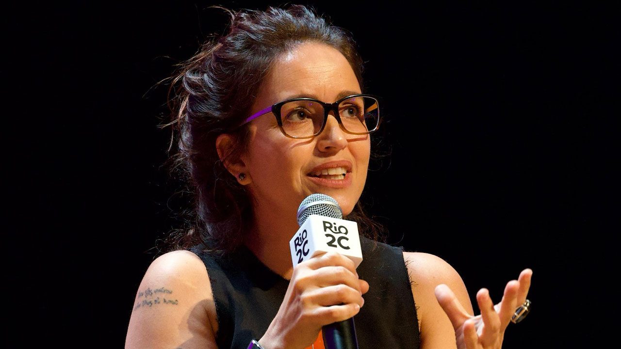 Manuela Dias fala ao microfone durante painel da Globo no evento Rio2C segurando microfone com logomarca do evento