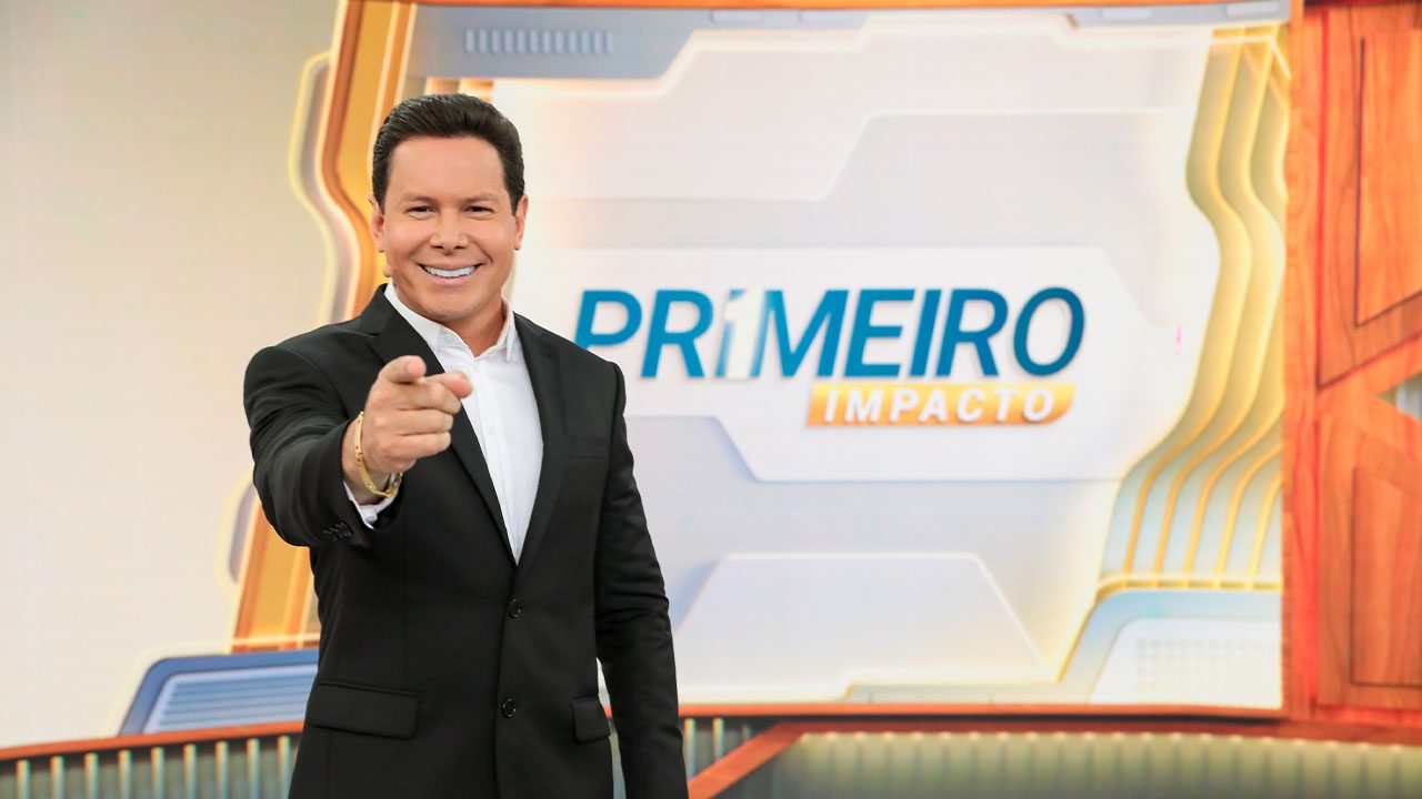 Marcão do Povo sorrindo e apontando para a câmera no estúdio do Primeiro Impacto do SBT