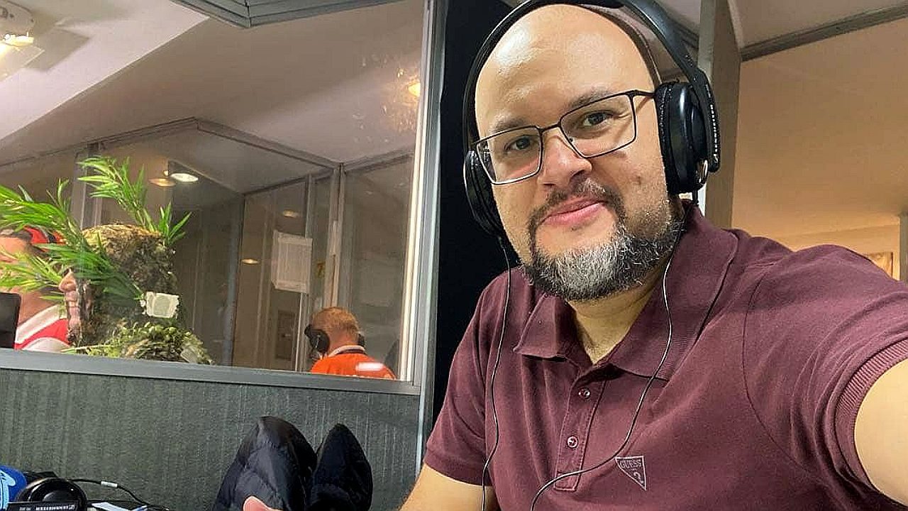 Marcelo do Ó usa fones de ouvido e posa na cabine de transmissão durante cobertura esportiva em estádio