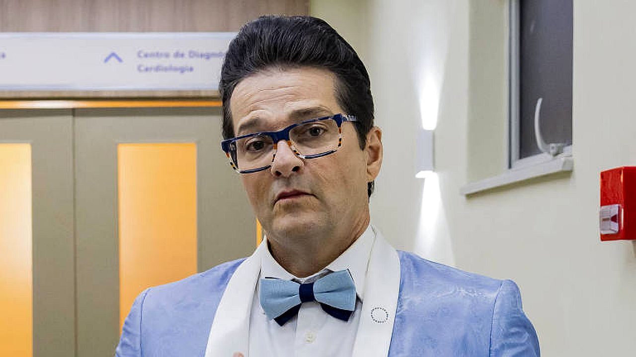 Homem de terno azul claro e gravata borboleta em corredor de hospital