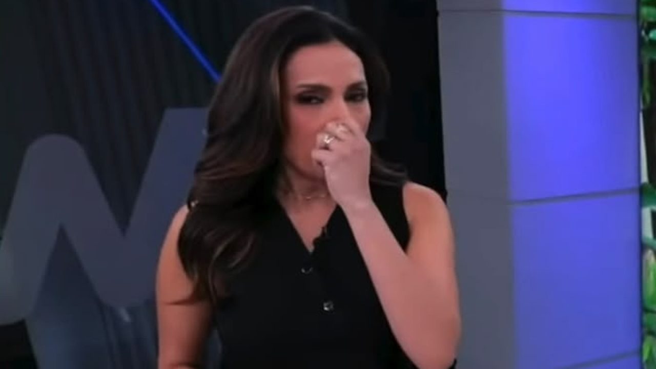 Márcia Dantas leva a mão ao rosto, com expressão de choro, no estúdio do Tempo Real