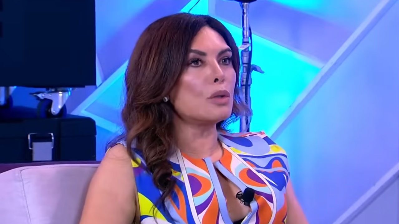Márcia Goldschmidt sentada em estúdio com iluminação azul durante entrevista na televisão