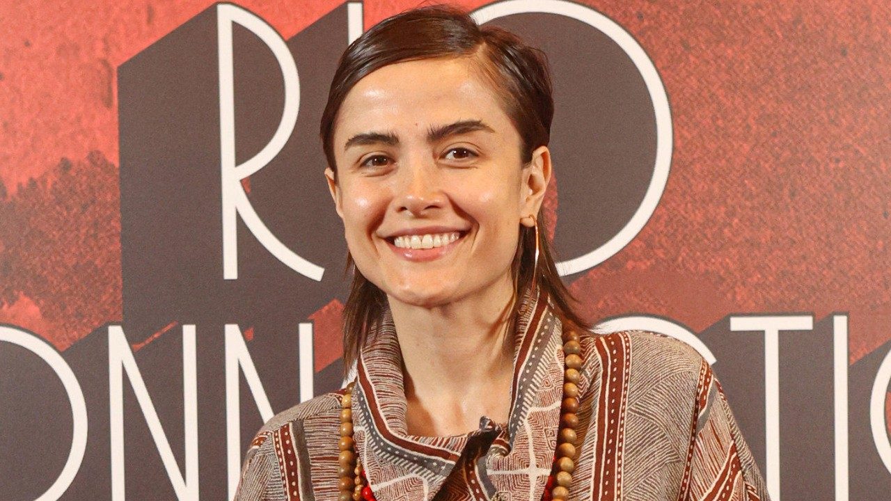 Maria Casadevall sorri diante de painel promocional durante evento de lançamento de série