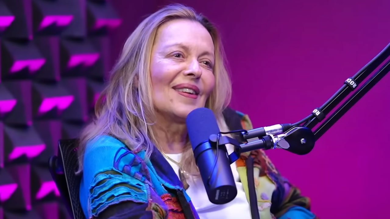 Maria Zilda Bethlem sorrindo durante entrevista em podcast com microfone à frente e fundo roxo iluminado