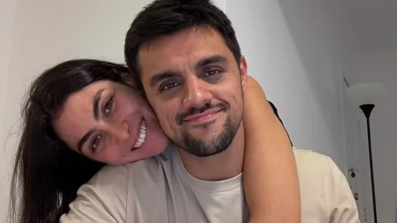 Mulher sorri enquanto abraça homem por trás em ambiente interno com iluminação suave