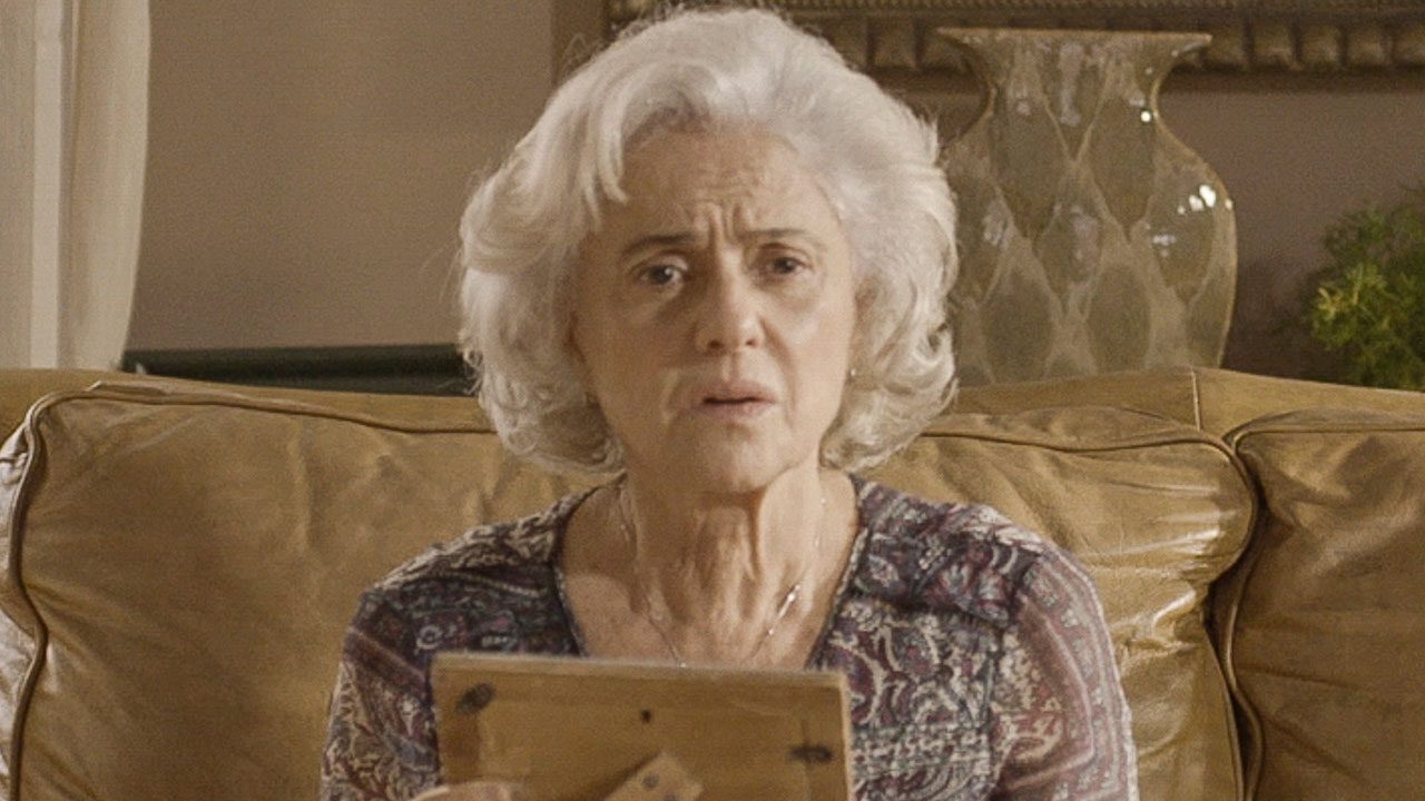 Marieta Severo como Noca sentada no sofá segurando porta-retrato em cena de Um Lugar ao Sol