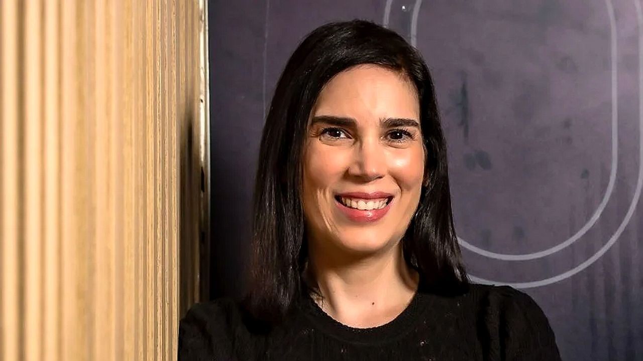 Marília Toledo sorri diante da câmera em retrato com blusa preta e fundo interno desfocado