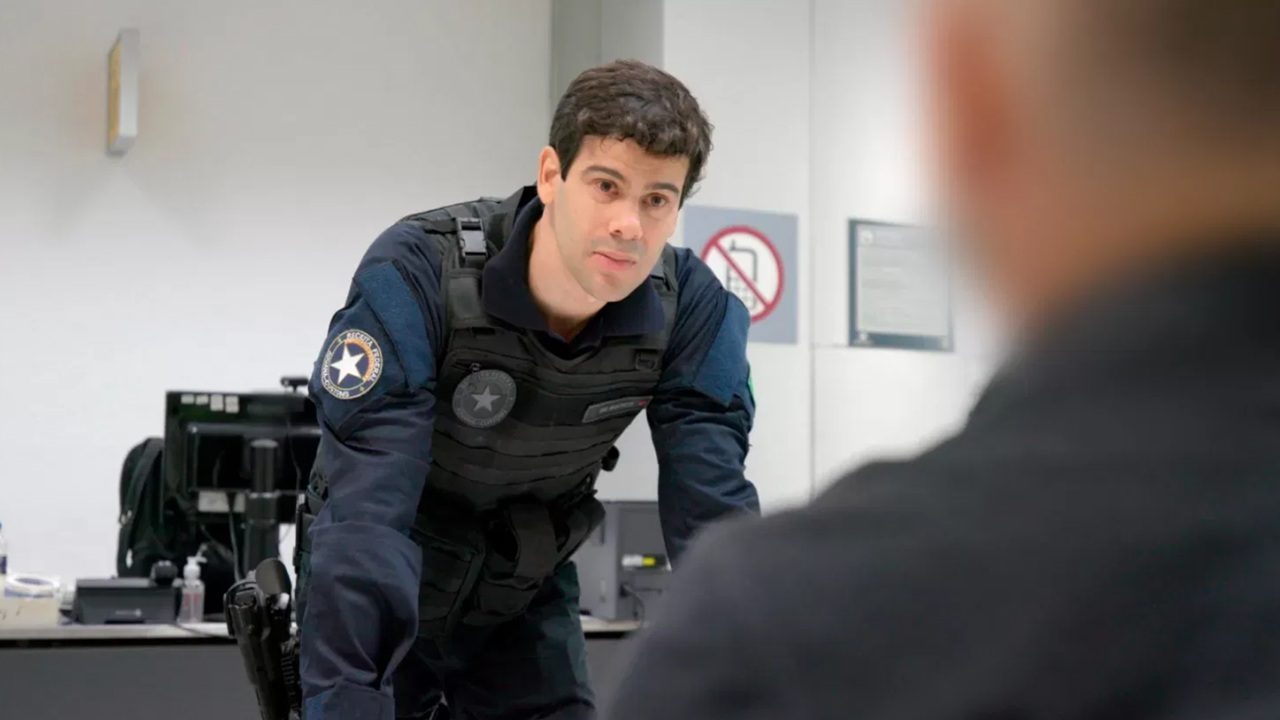 Mario de Marco como agente de segurança interroga passageiro em cena da série Aeroporto - Área Restrita