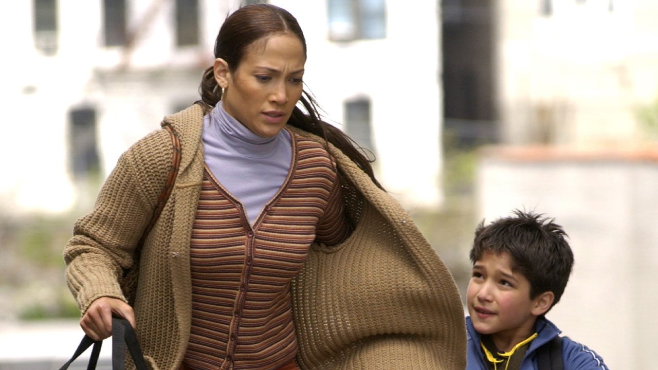A atriz Jennifer Lopez (Marisa Ventura) em casaco de tricô marrom e blusa lilás caminhando com seu filho Ty (Tyler Posey) na cena do filme Encontro de Amor