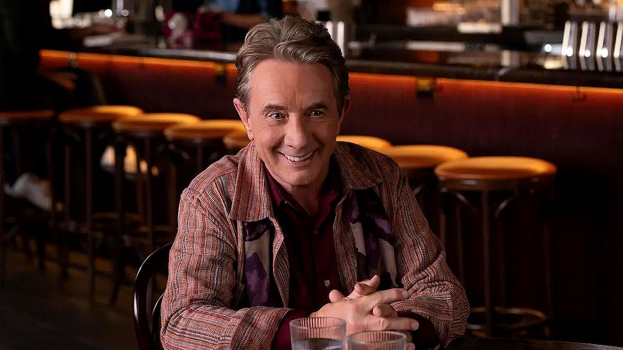 Personagem de Martin Short sorrindo em mesa de restaurante na série Only Murders in the Building