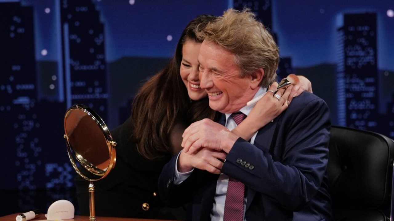 Mulher abraça homem sorridente em estúdio de programa de entrevistas, ambos demonstrando alegria e carinho