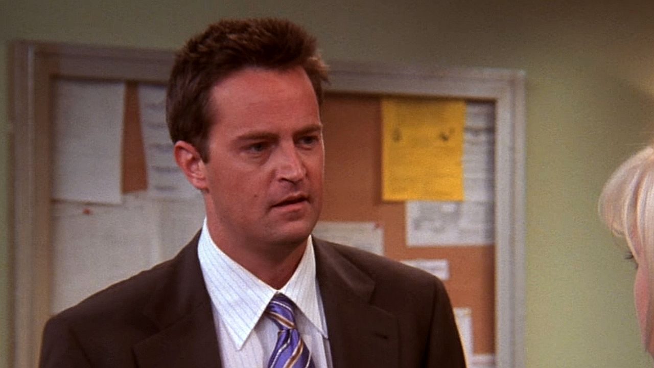 Matthew Perry de terno em cena da série Friends dentro de escritório da empresa Chandler Bing