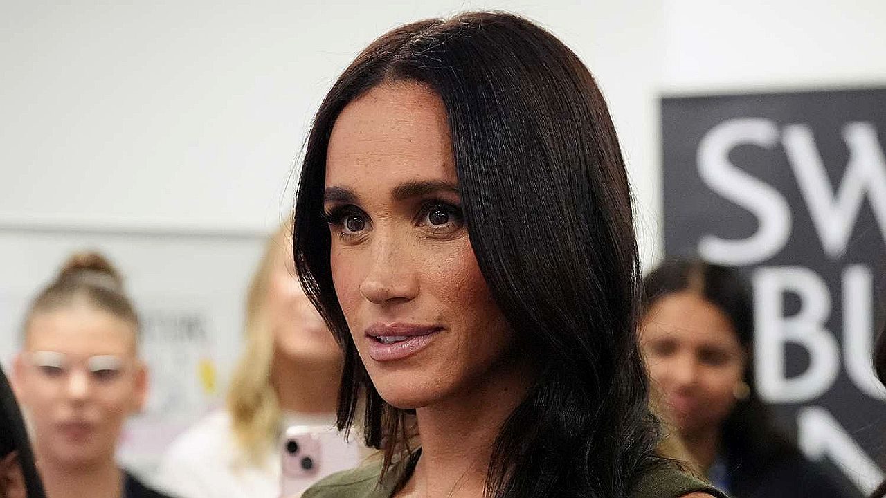 Meghan Markle observa com expressão atenta durante evento público com pessoas ao fundo