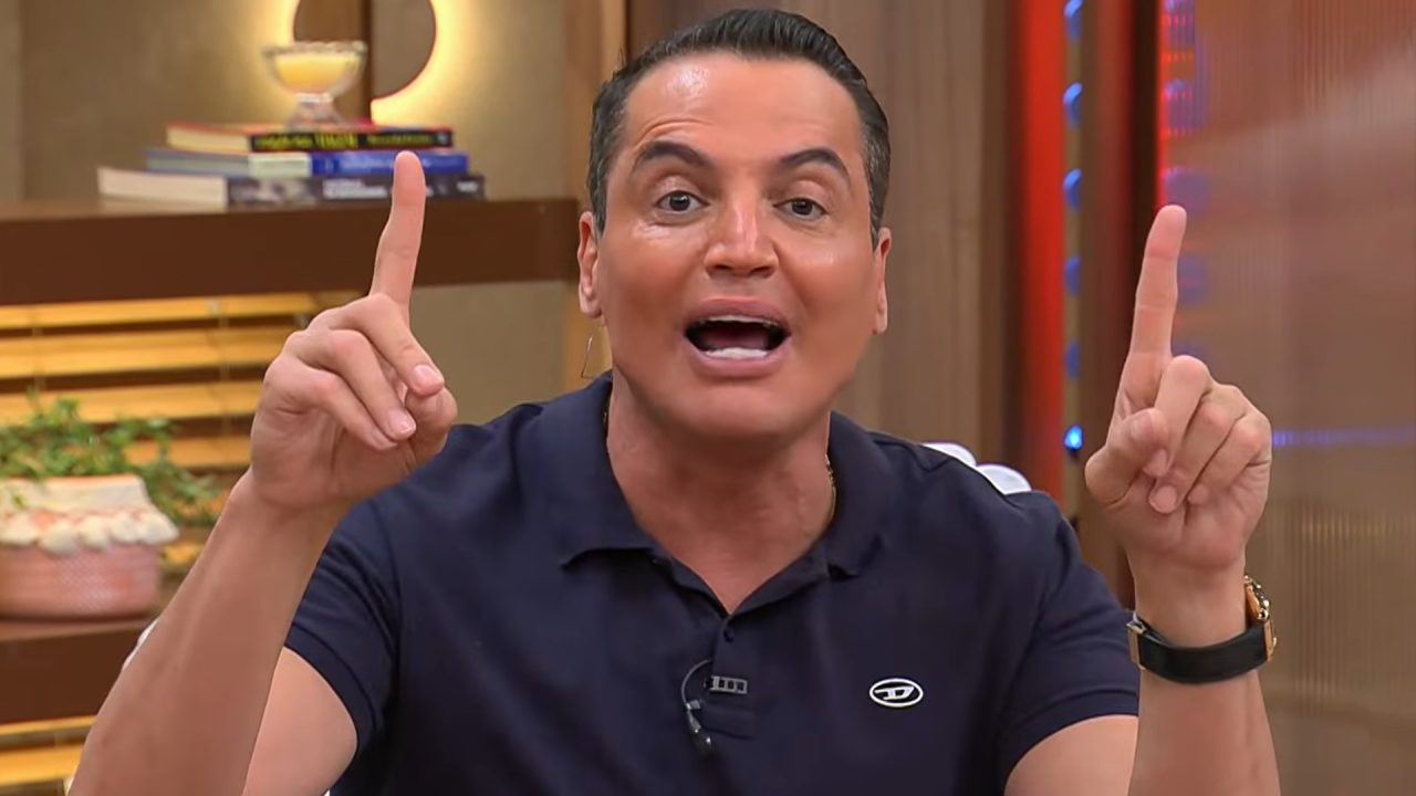 Leo Dias, apresentador do programa Melhor da Tarde, fala e gesticula com as mãos levantadas no estúdio da Band.