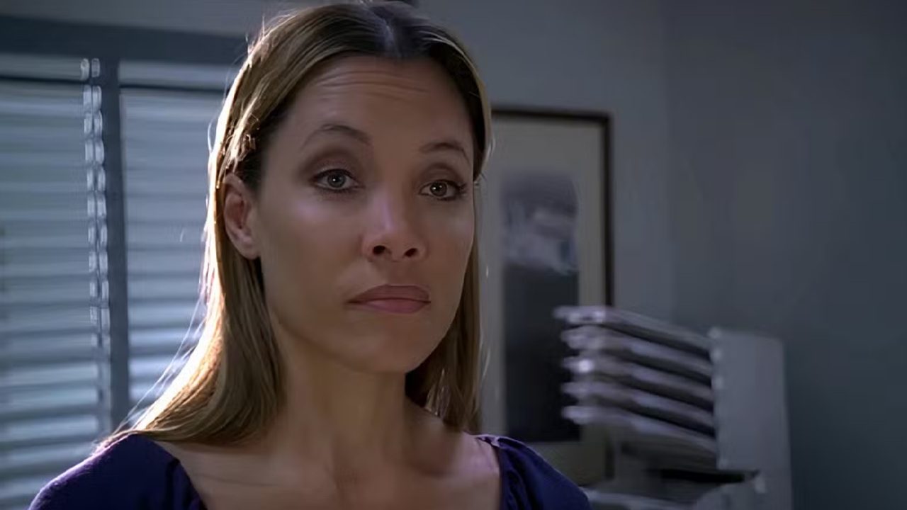 Mulher de expressão séria com blusa azul em ambiente interno iluminado por luz natural