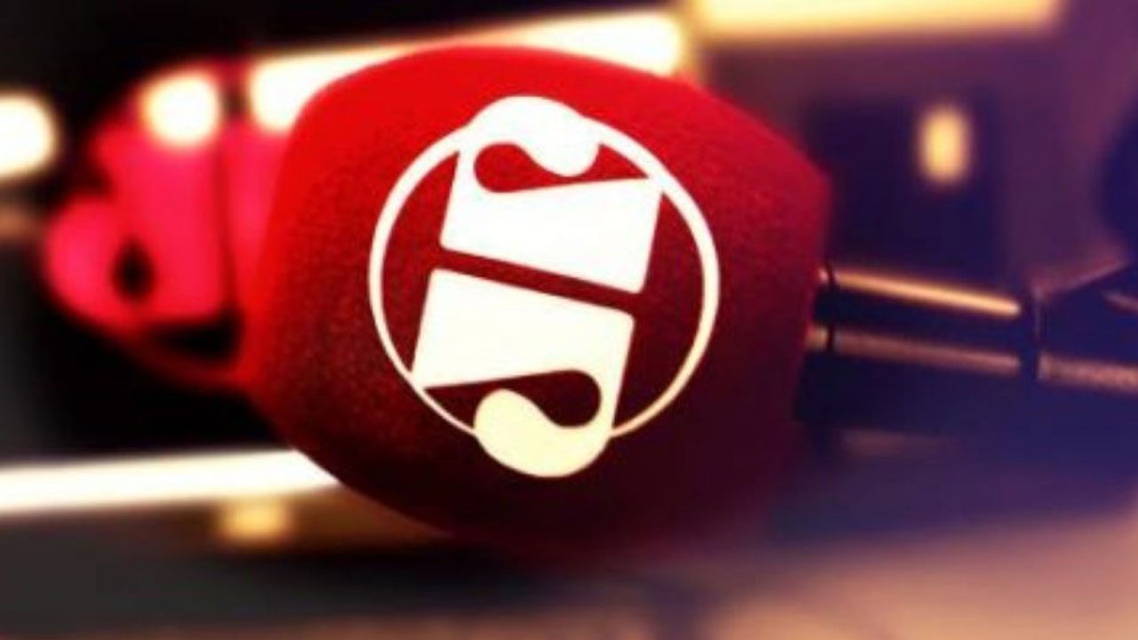 Microfone com espuma vermelha exibindo o logotipo da Jovem Pan em estúdio de rádio