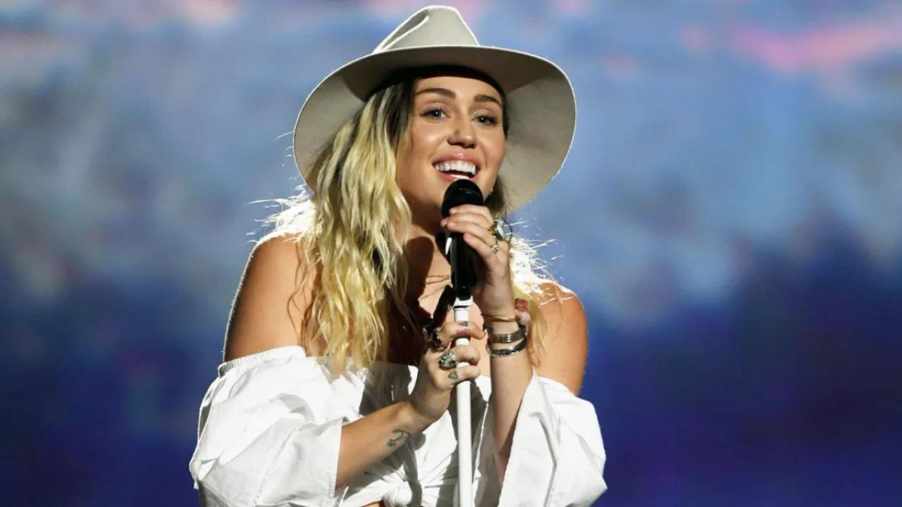 Foto de Miley Cyrus com uma blusa branca e um chapéu country