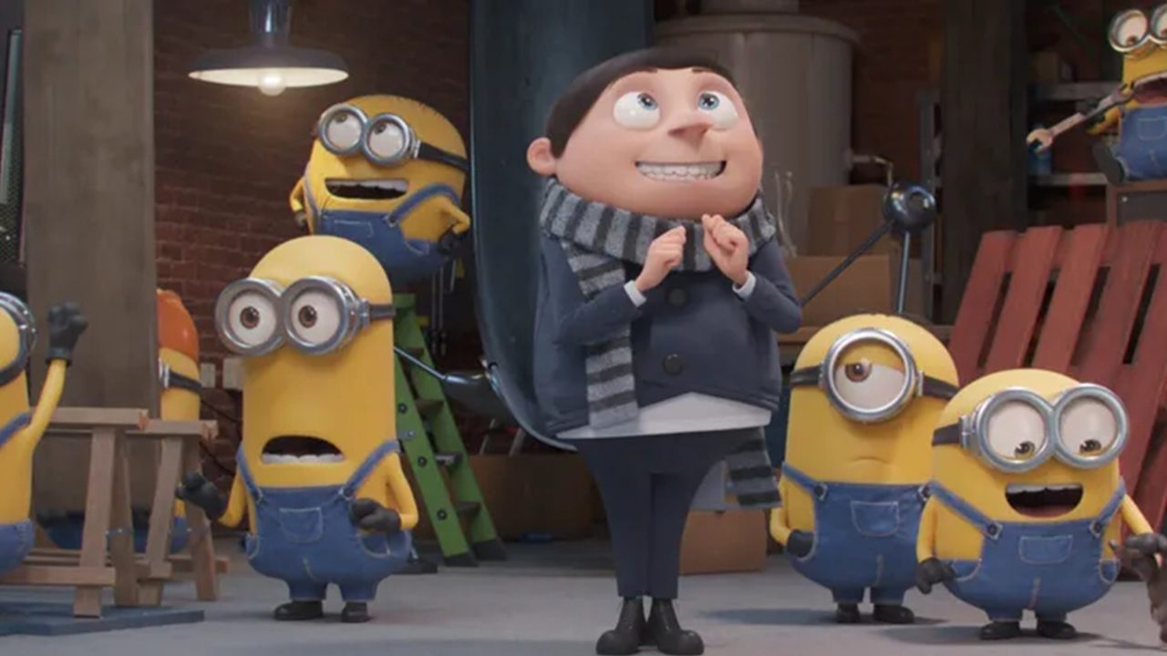 Cena animada mostra o jovem Gru cercado por vários Minions em um laboratório improvisado; ele sorri empolgado enquanto os pequenos personagens amarelos, usando macacões jeans e óculos de proteção, reagem com entusiasmo ao seu redor.