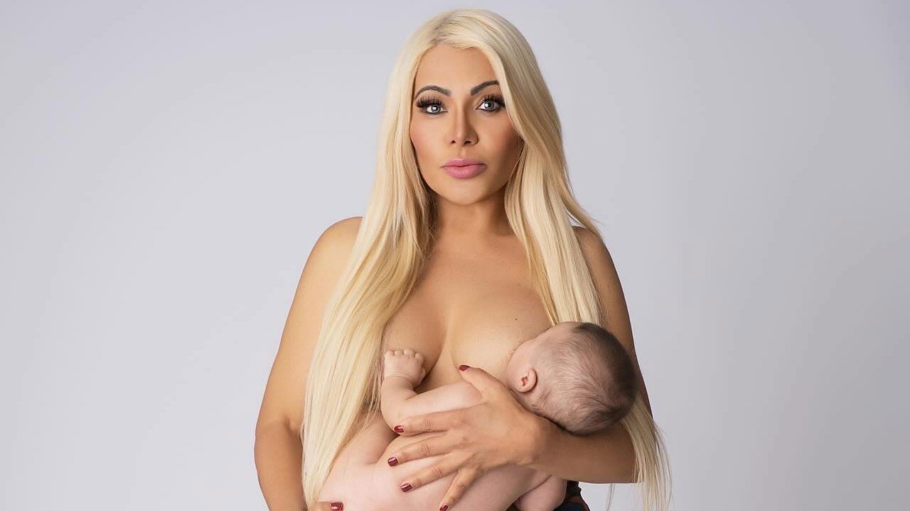 Mlow com cabelos longos e loiros amamentando um bebê em fundo neutro