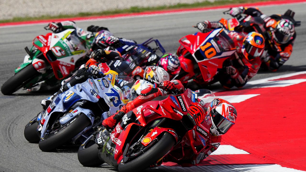 Pilotos de motovelocidade inclinam suas motos coloridas de alta cilindrada durante uma curva acentuada em circuito de corrida da MotoGP