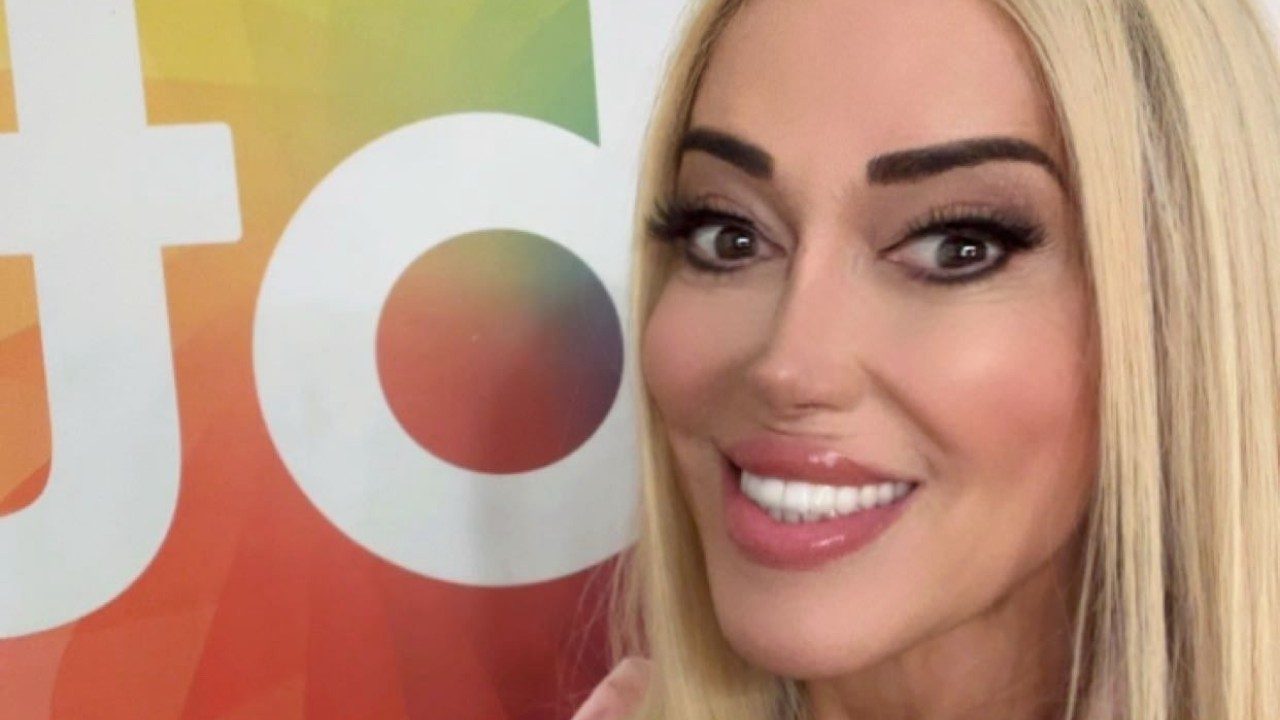 Mulher Abacaxi sorri em selfie diante de painel colorido com logotipo do SBT ao fundo