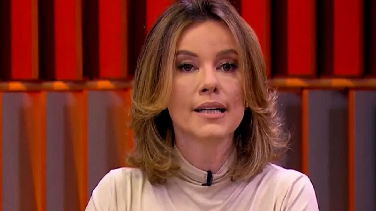 Mulher fala durante programa de TV com cenário em tons de vermelho ao fundo