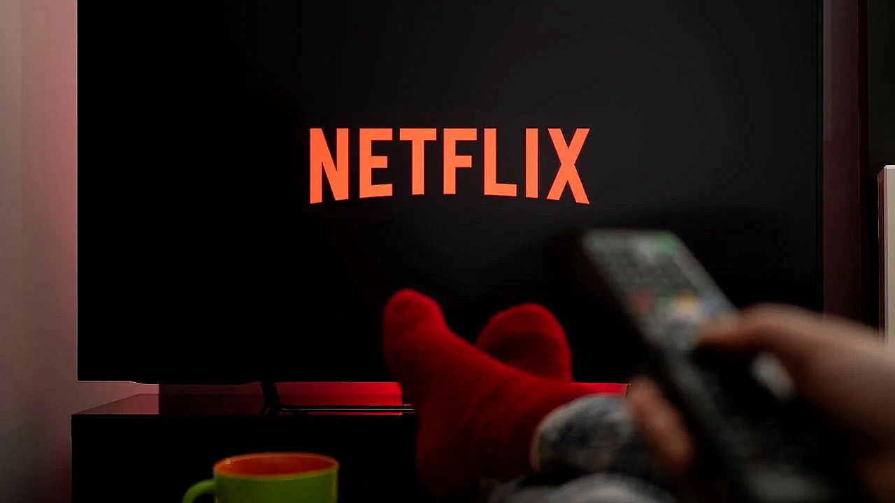 Logotipo da Netflix exibido na televisão enquanto pessoa segura controle remoto na sala escura