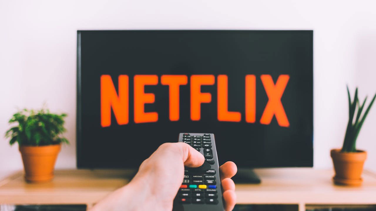 Pessoa apontando controle remoto para televisão com logotipo da Netflix em destaque na tela