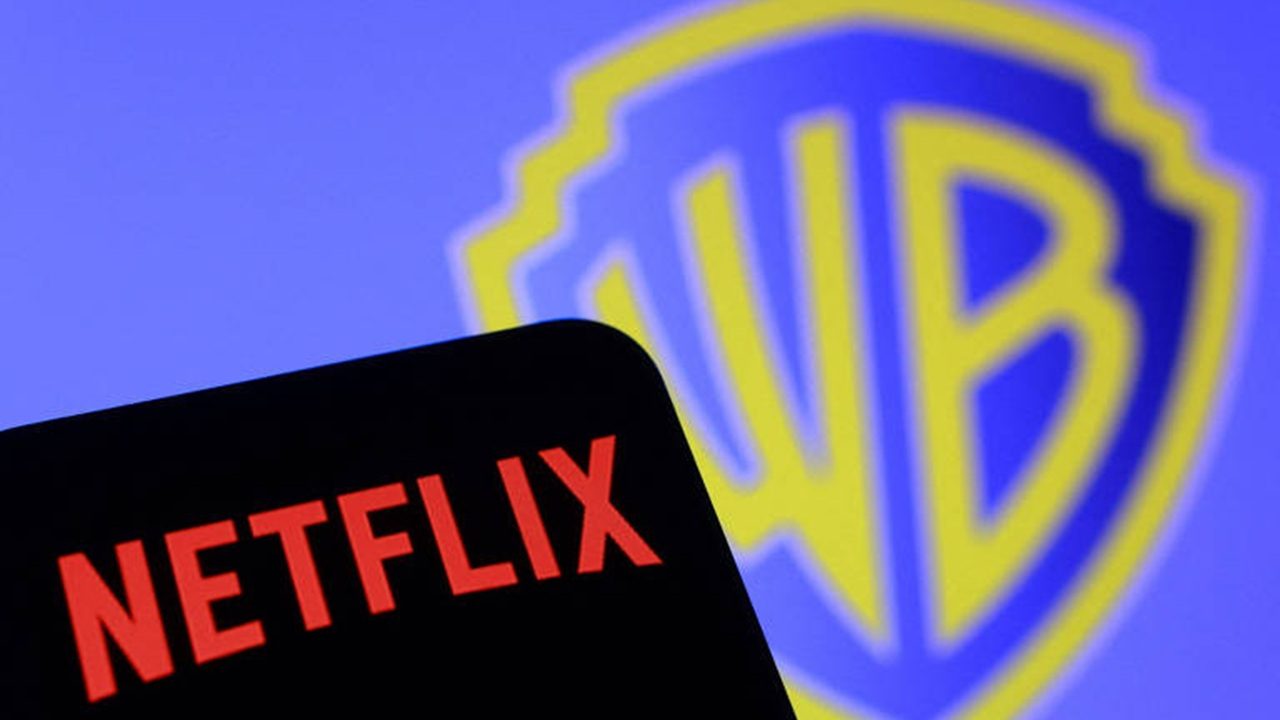 Close de uma tela exibindo o logo vermelho da Netflix em um dispositivo móvel, com o logotipo desfocado da Warner Bros. em azul e amarelo ao fundo
