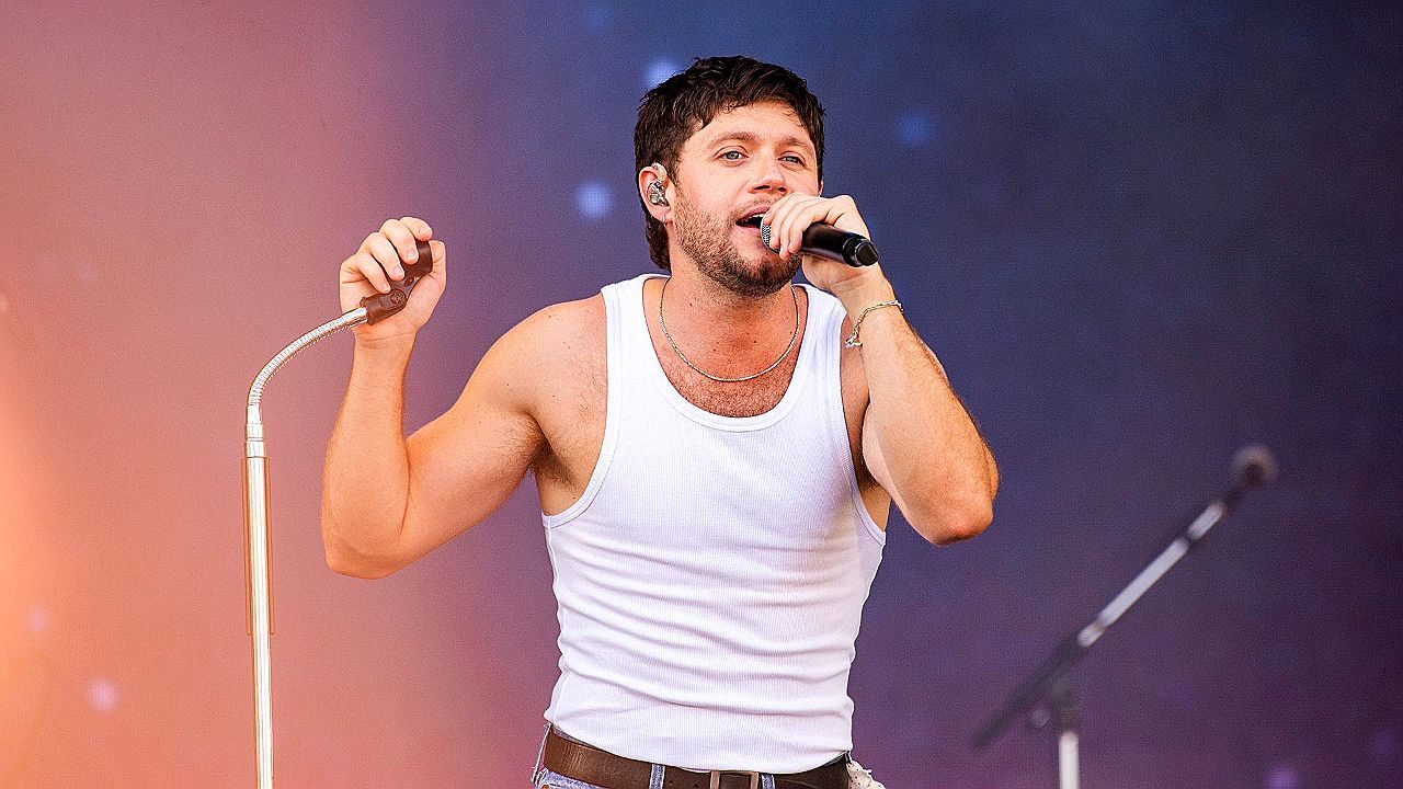 Cantor se apresenta no palco com microfone durante show ao vivo vestindo regata branca