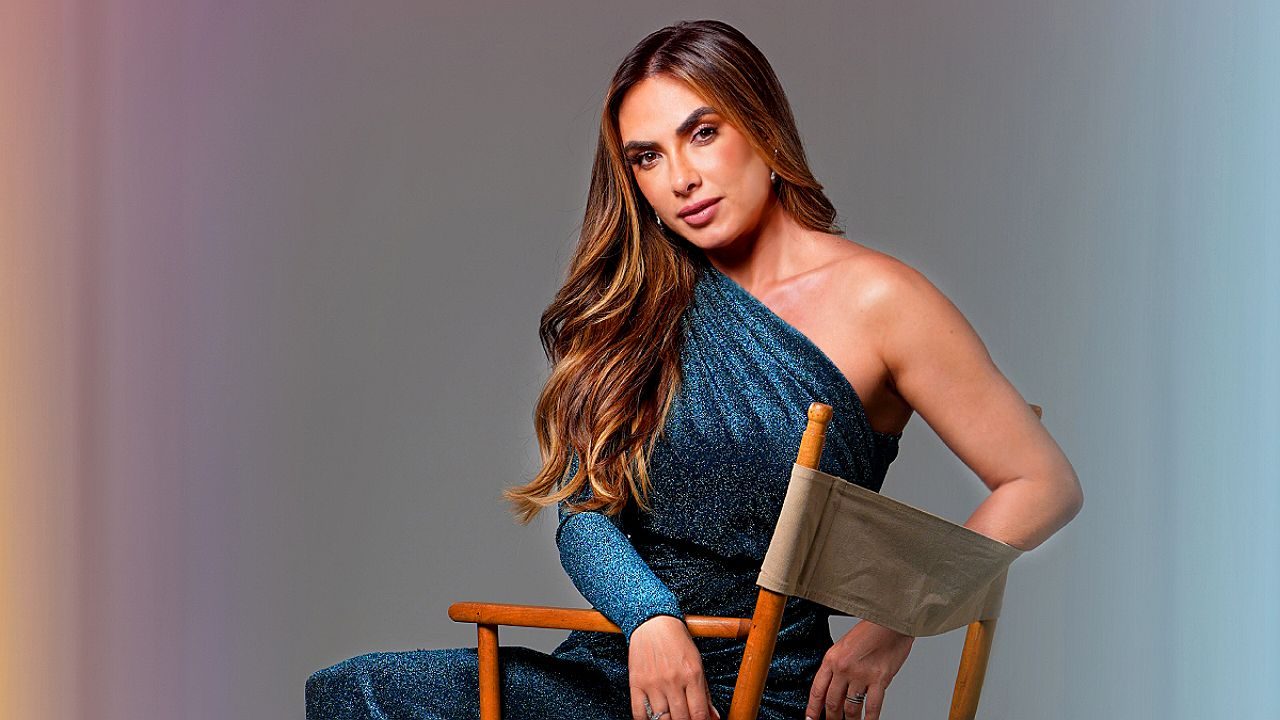 Nicole Bahls posa sentada em cadeira de diretor usando vestido azul de um ombro só em ensaio fotográfico