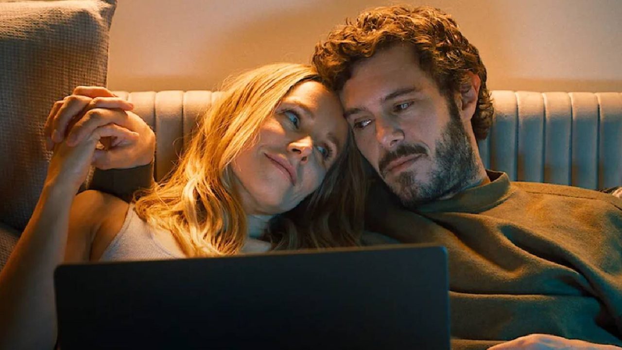 Casal deitado no sofá assiste algo em um laptop, trocando olhares carinhosos sob luz suave e ambiente acolhedor