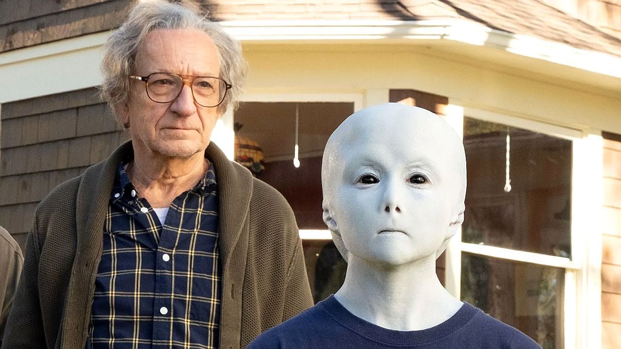 Homem idoso ao lado de figura humanoide branca com rosto sem expressão em cena de série de ficção científica