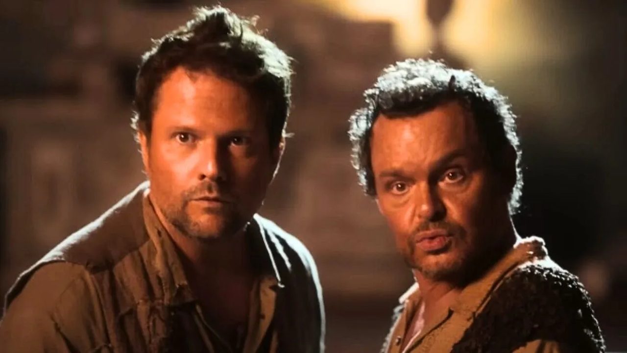 Dois homens com expressão de surpresa e roupas rústicas observam algo fora de cena em ambiente iluminado por luz amarelada