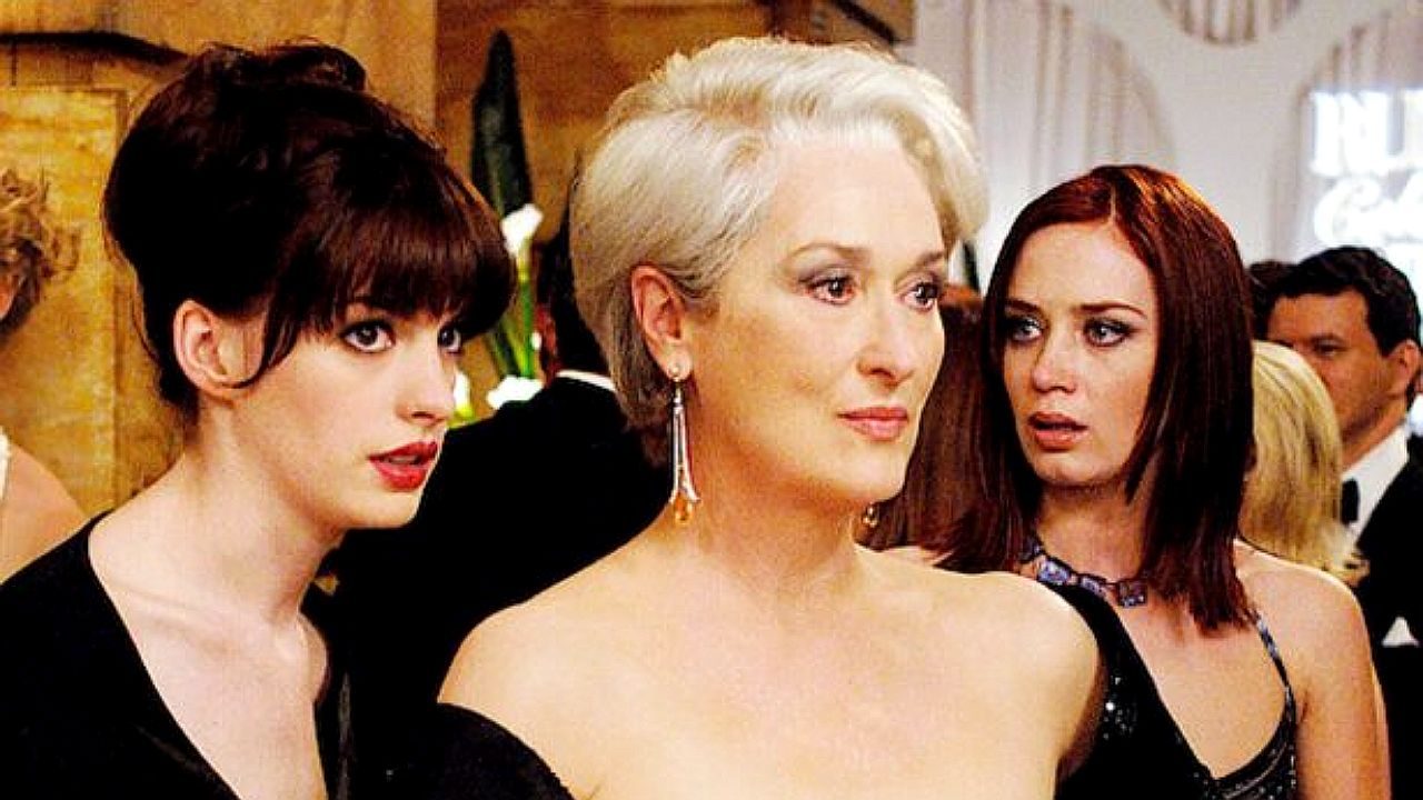 Miranda Priestly observa séria enquanto Andy Sachs e Emily Charlton reagem em cena de O Diabo Veste Prada
