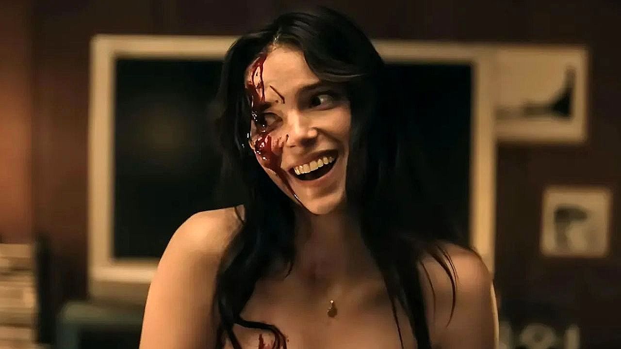Mulher com metade do rosto ensanguentada sorri em cena da série Obsessão com clima de terror psicológico
