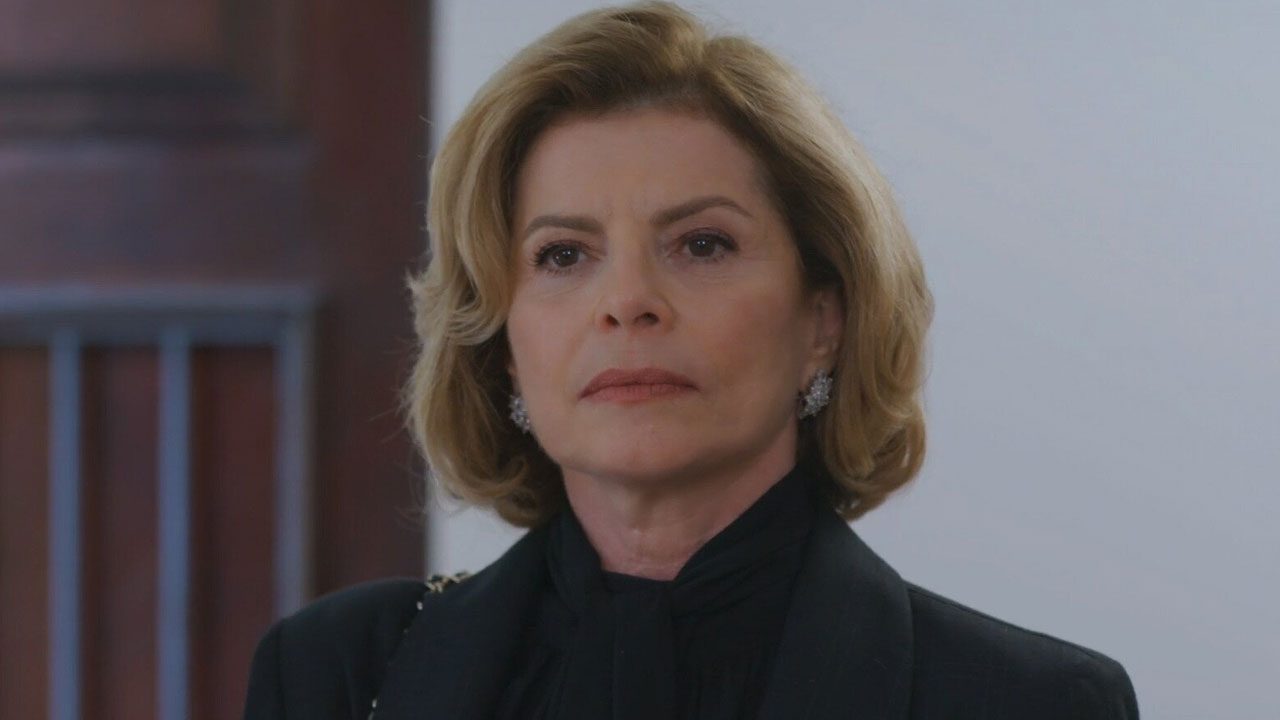 Débora Bloch caracterizada como Odete Roitman usa roupa preta e brincos brilhantes em cena do remake da novela Vale Tudo