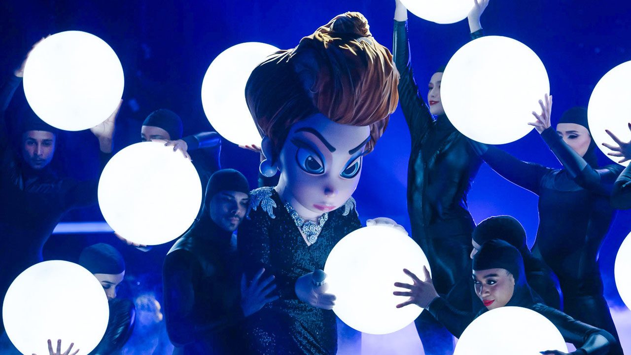 Personagem Odete Roitman cercada por dançarinos com globos iluminados no palco do The Masked Singer Brasil da Globo