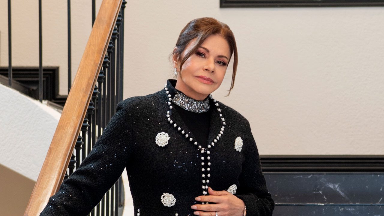 Ofélia Garcia (Maria Sorté) de casaco preto com pérolas encostada no corrimão em cena de As Filhas da Senhora Garcia