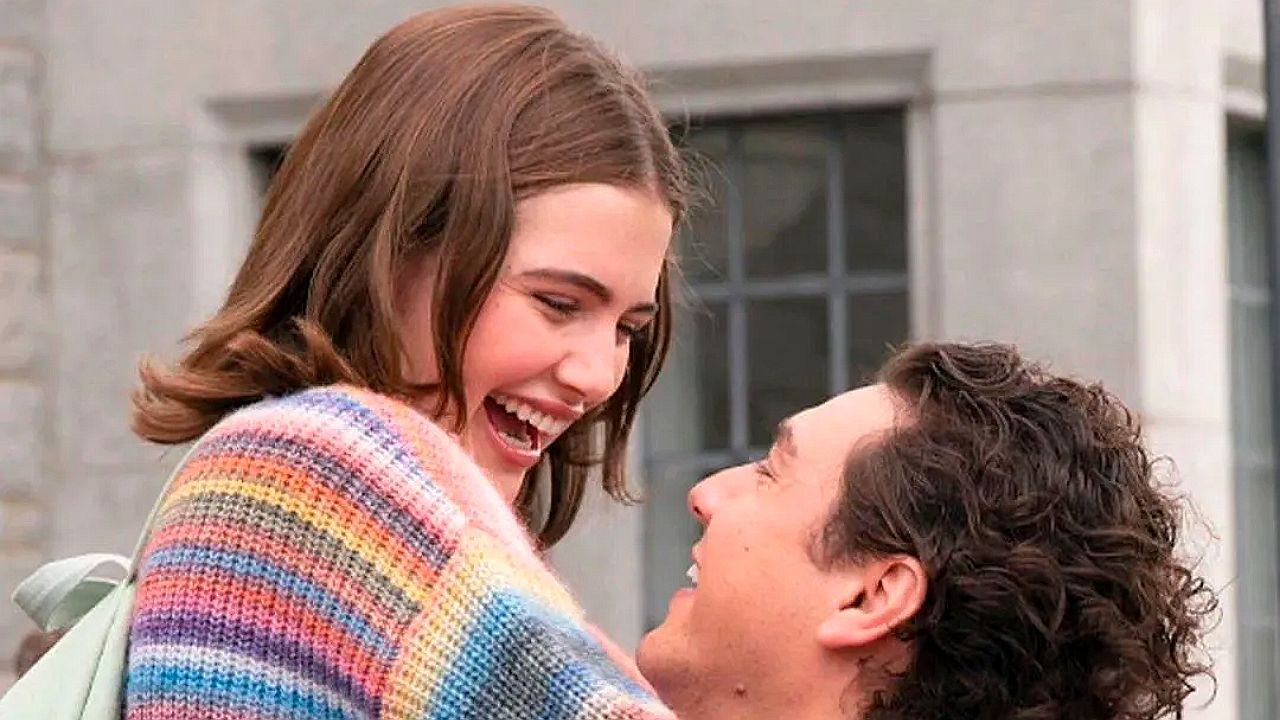 Casal se abraça sorrindo em cena da série Off Campus diante de prédio universitário ao fundo