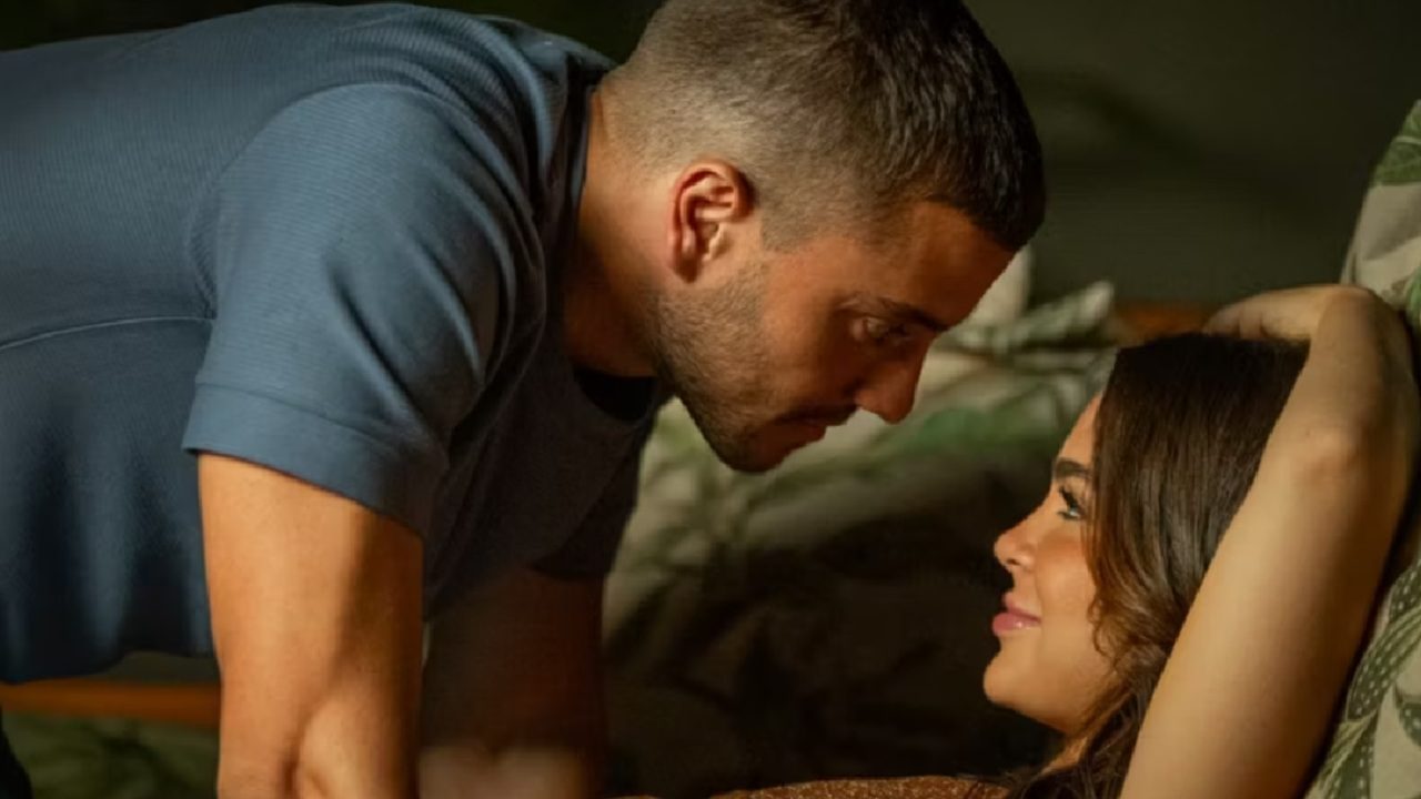 Atores de Os Donos do Jogo trocam olhares próximos e intensos em um ambiente íntimo, com iluminação suave e expressão de carinho e conexão entre eles