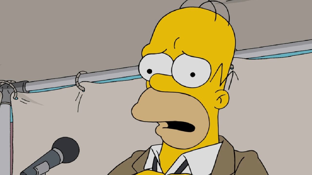 Cena da animação Os Simpsons, mostrando o personagem Homer Simpson com expressão preocupada diante de um microfone, em um ambiente interno iluminado
