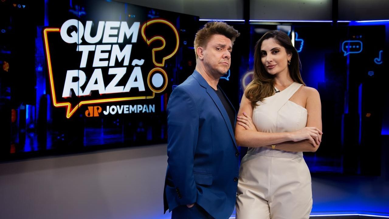 Oscar Filho de terno azul e Paula Nobre de macacão claro posam de braços cruzados em estúdio diante do telão com logo do programa Quem Tem Razão?