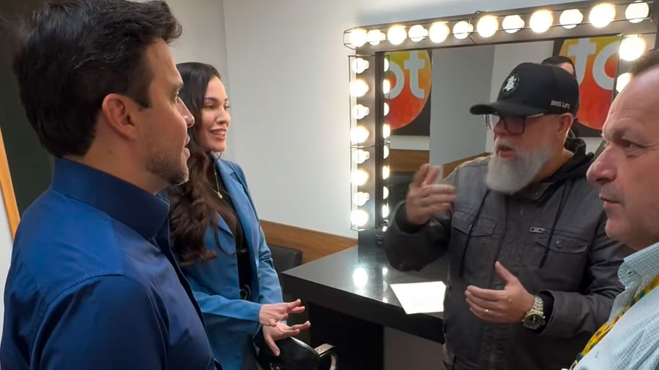 Pablo Marçal conversa com diretores do SBT em camarim iluminado com espelho e logotipo da emissora ao fundo